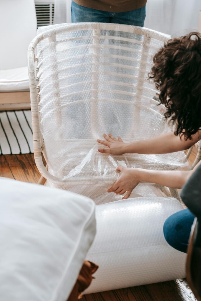 A woman carefully wraps a chair in bubble wrap to prepare for moving or relocation.
